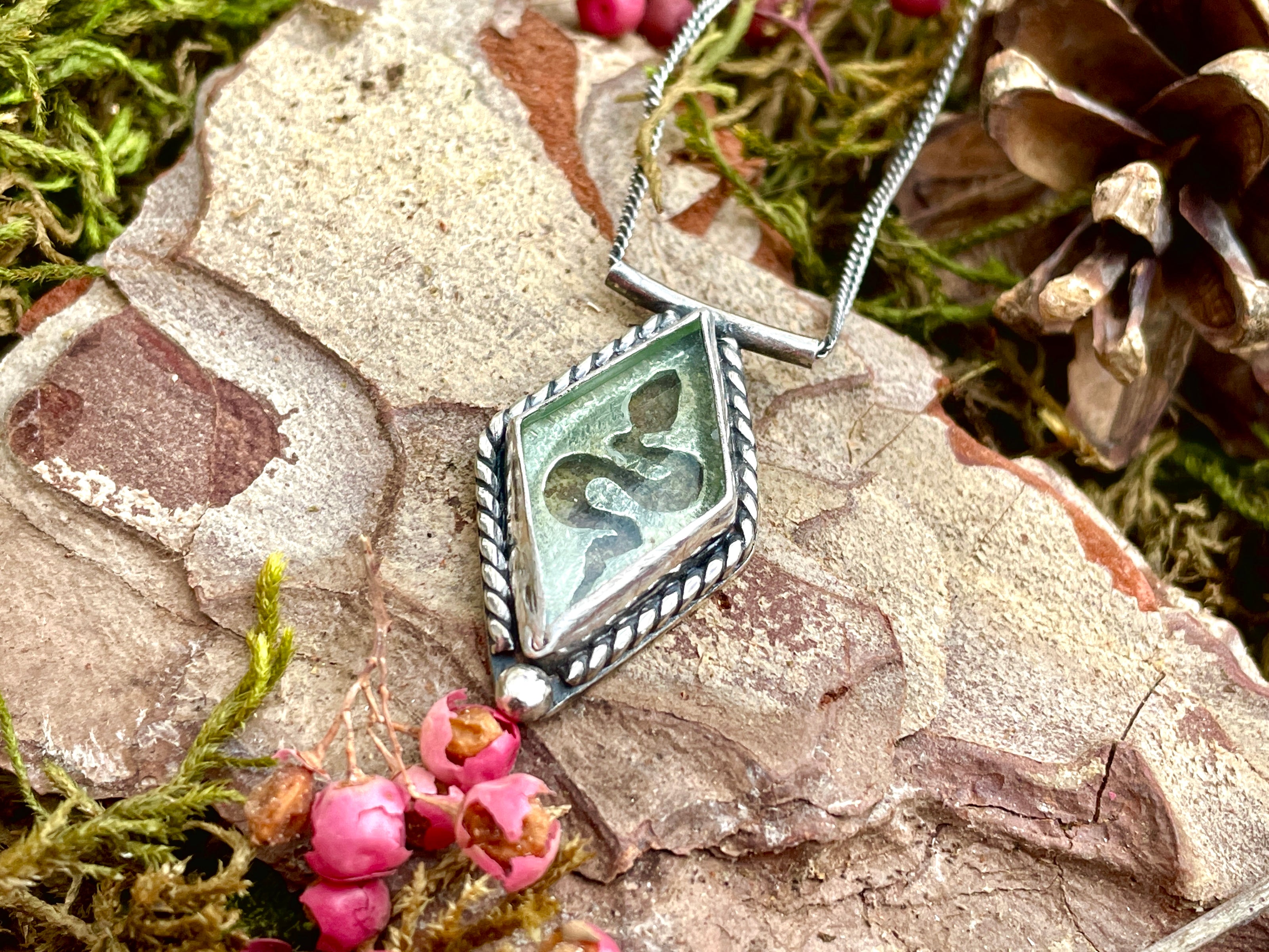 A bespoke necklace made in silver sterling, featuring a diamond shaped uranium glass cabochon with a cut out of a snake underneath